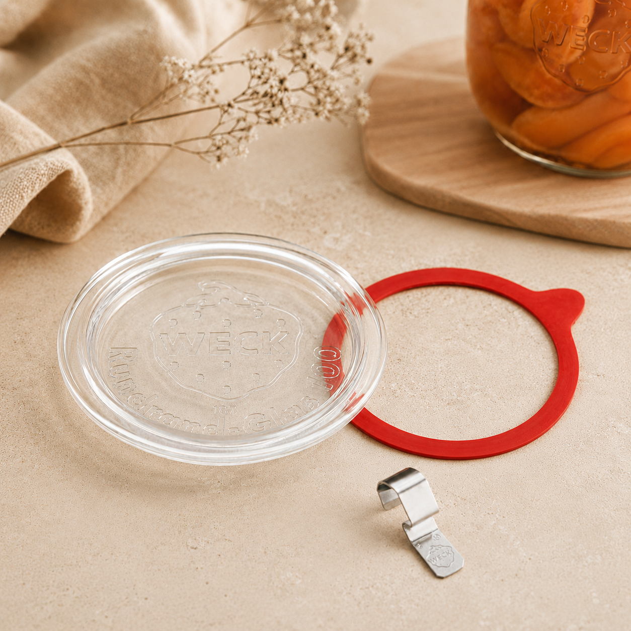 WECK-Glasdeckel mit rotem Gummiring und Metallklammer, dekorativ angeordnet in einer warmen, beigen Küchenatmosphäre
